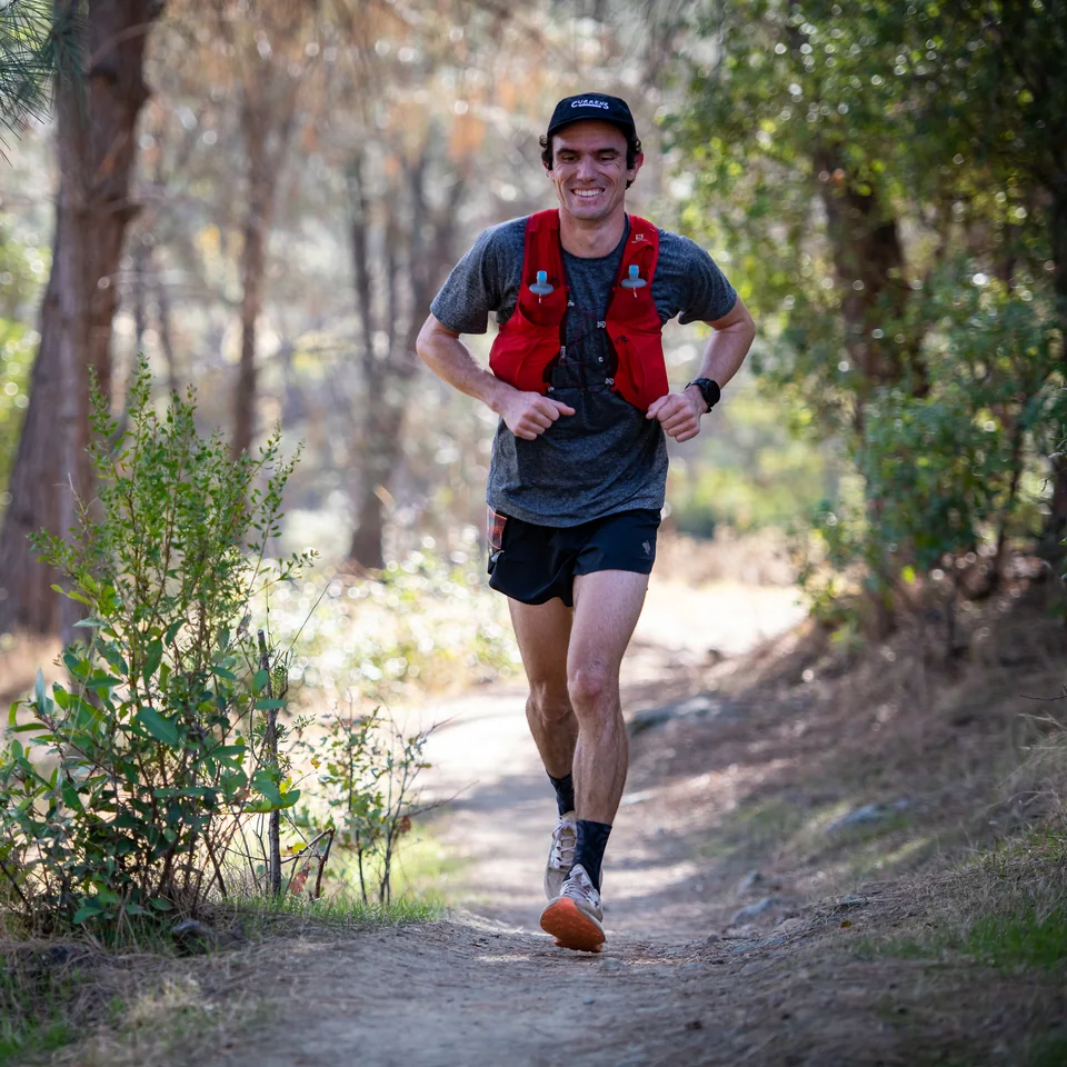 Brandon Costa running through woodland in a red hydration vest.