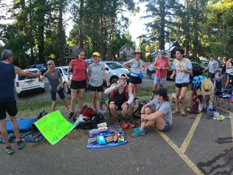 Group gathered beside chairs, bags and supplies on a tree-lined roadside at Foresthill.