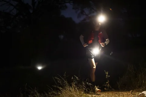 Runner wearing a bright headlamp on a dark trail at night.