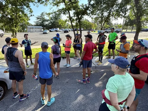 Group in running clothes gathered in a circle in a tree-lined parking lot.