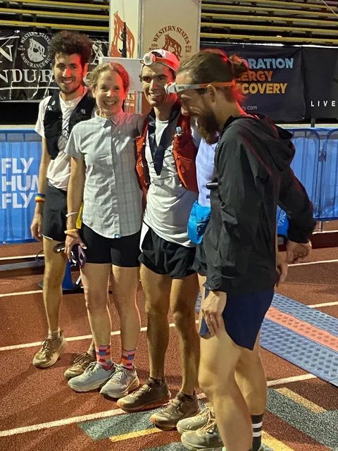 Four people posing together on a running track beside Western States finish-area banners.