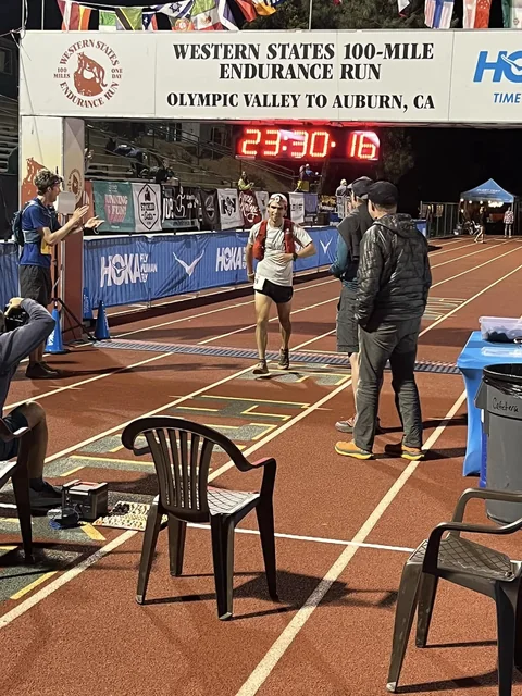 Runner on a track beneath the Western States 100-Mile Endurance Run finish banner at night.